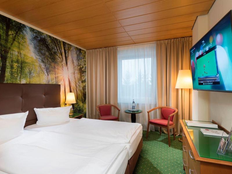Modernes Hotelzimmer mit Doppelbett, Wandbild, zwei Sesseln und TV an der Wand.
