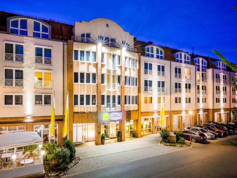 Beleuchtetes mehrstöckiges Hotel bei Nacht mit geparkten Autos davor.