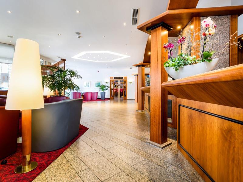 Helle Hotellobby mit modernem Sofa, Stehlampe und dekorativem Blumenarrangement.