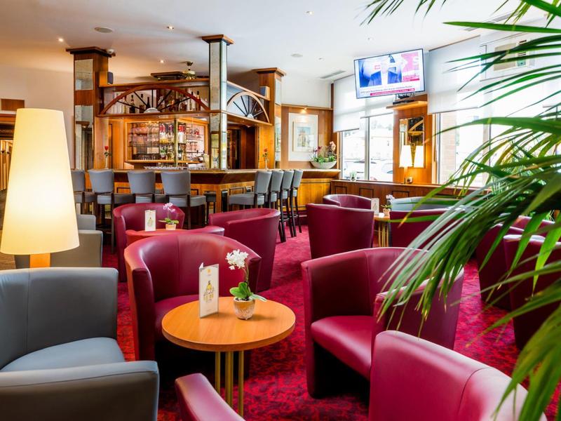 Gemütliche Hotellounge mit roten Sesseln, runden Tischen und einer Bar im Hintergrund.