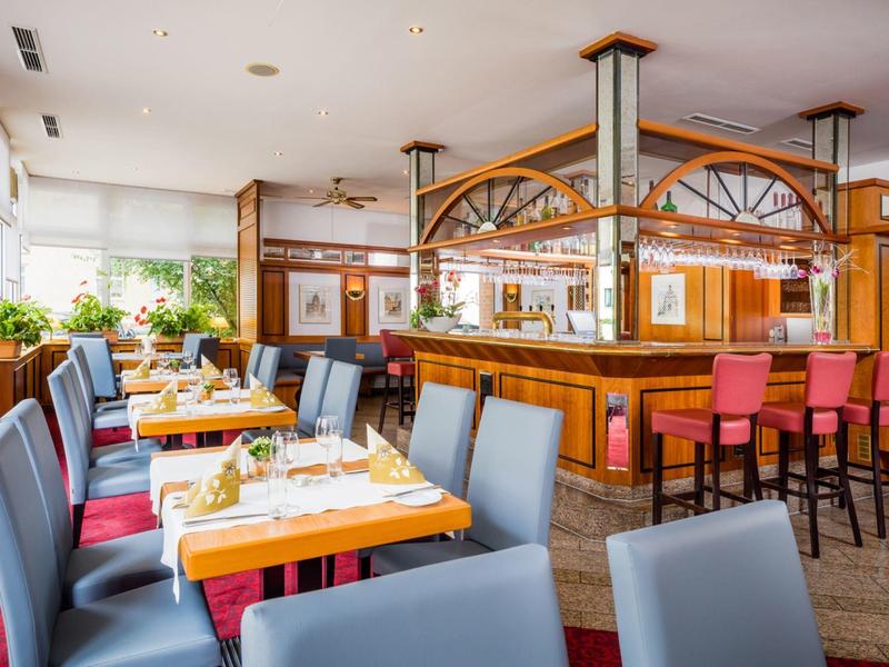 Helles Restaurantinterieur mit Holzmöbeln, blauen und roten Stühlen und gedeckten Tischen.