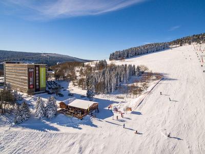 Schneebedecktes Hotel mit Skihang und Wald bei klarem Himmel.