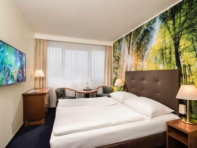 Gemütliches Hotelzimmer mit Doppelbett, Baumwandbild und Fernseher an der Wand.