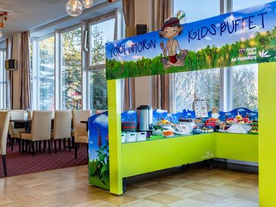 Bunt dekoriertes Kinderbuffet in einem hellen Restaurant mit großen Fenstern und moderner Einrichtung.