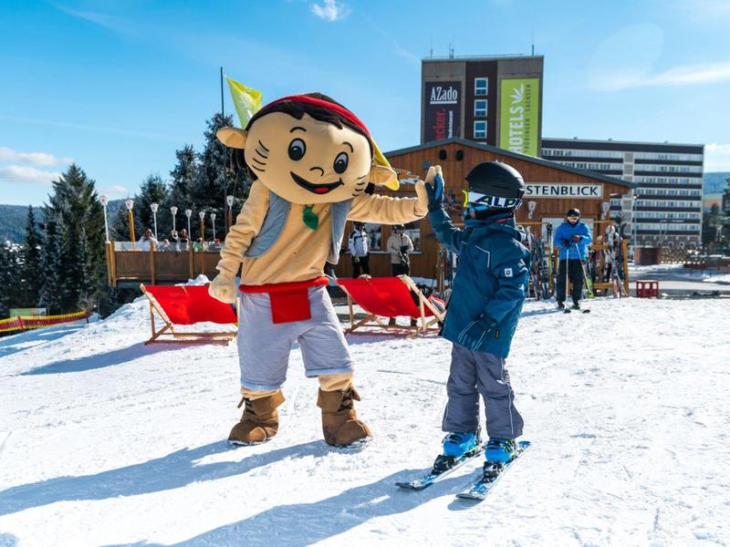 A child greets a person in a fun mascot costume on a snowy ski slope.