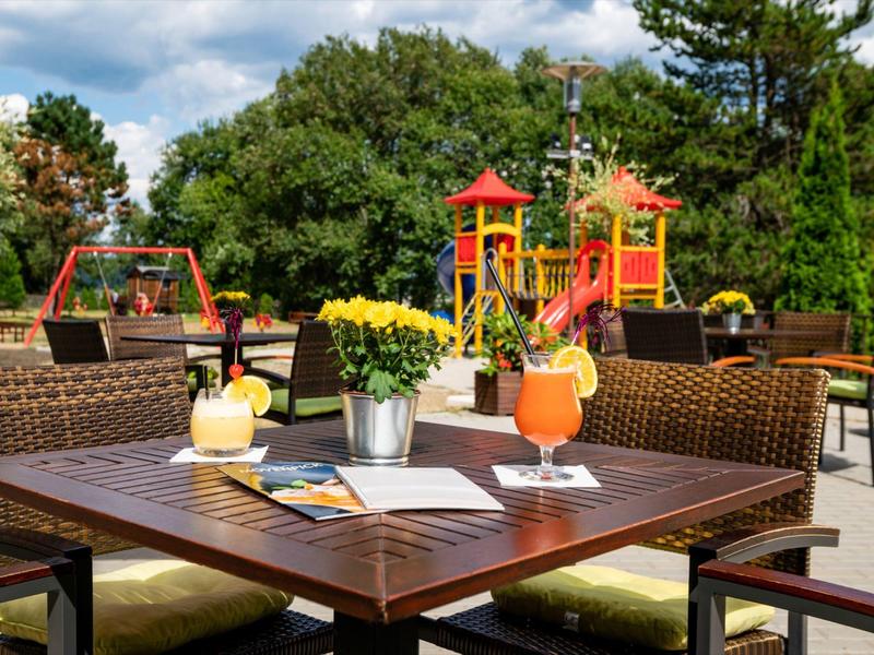 Picnic table with drinks in front of a colorful children's playground in a park.