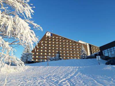 Grand bâtiment d'hôtel sous la neige avec un ciel bleu clair et des arbres enneigés.