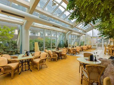 Véranda lumineuse avec mobilier en rotin et de nombreuses plantes dans un hôtel.