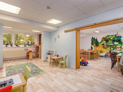 Salle de jeux et d'apprentissage lumineuse et spacieuse avec tables, chaises d'enfants et décorations murales.