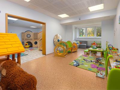 Espace de jeux pour enfants lumineux avec jouets, tapis et un grand ours en peluche dans une chambre d'hôtel.