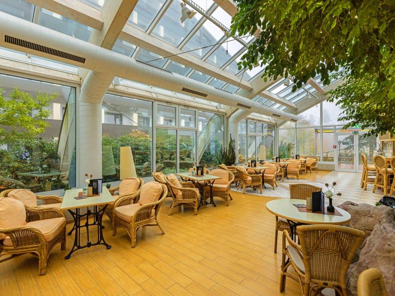 Véranda lumineuse avec mobilier en rotin et de nombreuses plantes dans un hôtel.