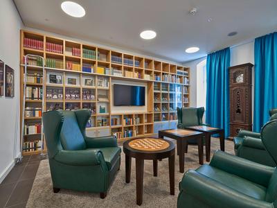 Gemütlicher Lese- und Aufenthaltsraum mit Büchern, Fernseher und grünen Sesseln.