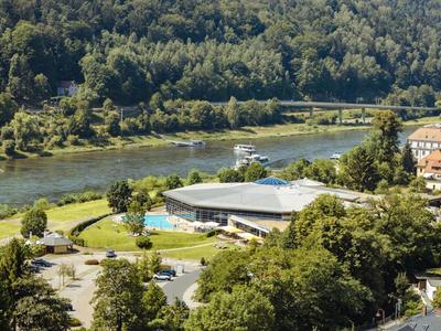 Landschaft mit einem Fluss, Wald, einem modernen Gebäude und Parkplätzen in einer grünen Umgebung.