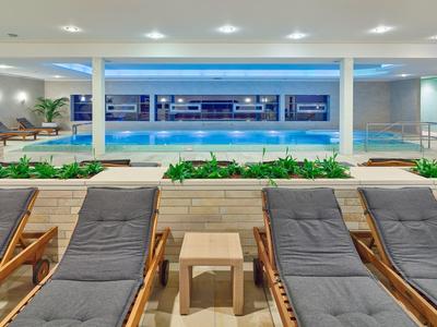 Hallenbad mit Liegestühlen und Pflanzen in moderner Hotelumgebung