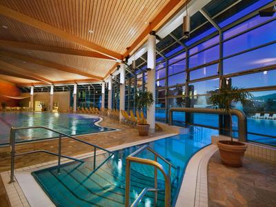 Modernes Hallenbad mit Glasfront und Stadtblick bei Dämmerung im Hotel.