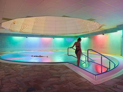 Innen beheizter Poolbereich mit farbig beleuchteten Wänden und einer Person am Treppengeländer.