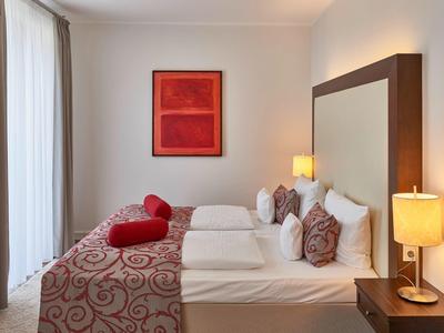 Modern eingerichtetes Hotelzimmer mit Doppelbett, roten Akzenten und zwei Nachttischlampen.