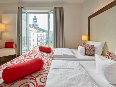 Modern eingerichtetes Hotelzimmer mit zwei Betten, großen Fenstern und Blick auf Stadtgebäude.