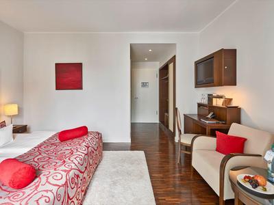 Helles Hotelzimmer mit Doppelbett, Schreibtisch, zwei Stühlen und roter Dekoration.