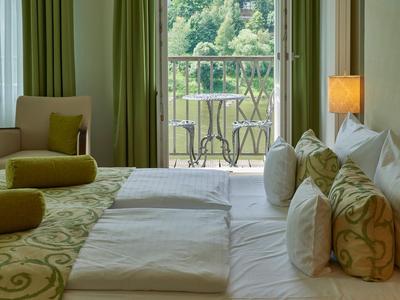 Gemütliches Hotelzimmer mit großen Betten, Sitzbereich und Balkon mit Blick auf grüne Landschaft.