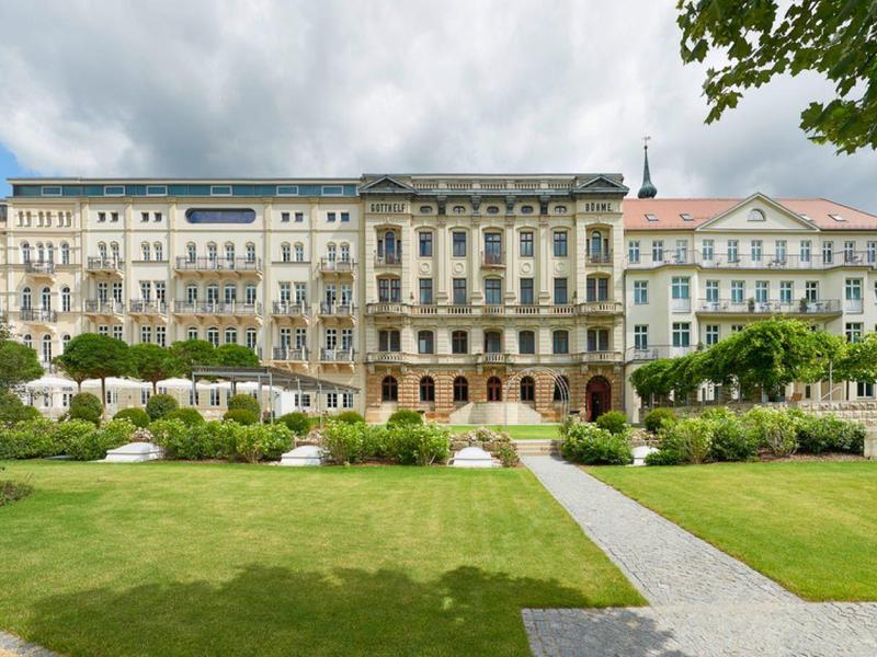 Großes historisches Hotelgebäude mit gepflegtem Garten und Wegen im Vordergrund.
