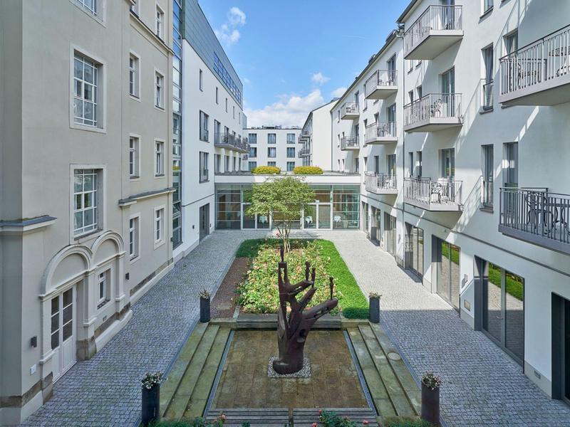 Innenhof eines modernen Hotels mit Skulptur, Garten und Balkonen unter blauem Himmel