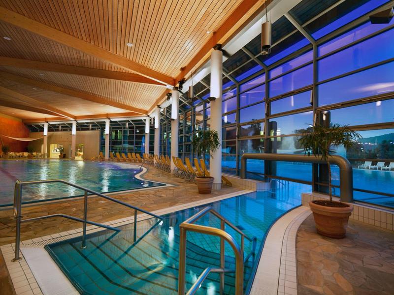 Modernes Hallenbad mit Glasfront und Stadtblick bei Dämmerung im Hotel.