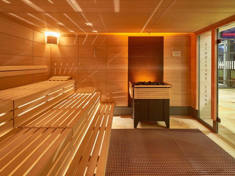 Moderne Sauna mit Holzbänken, elektrischem Ofen und Glastür zum Außenbereich.