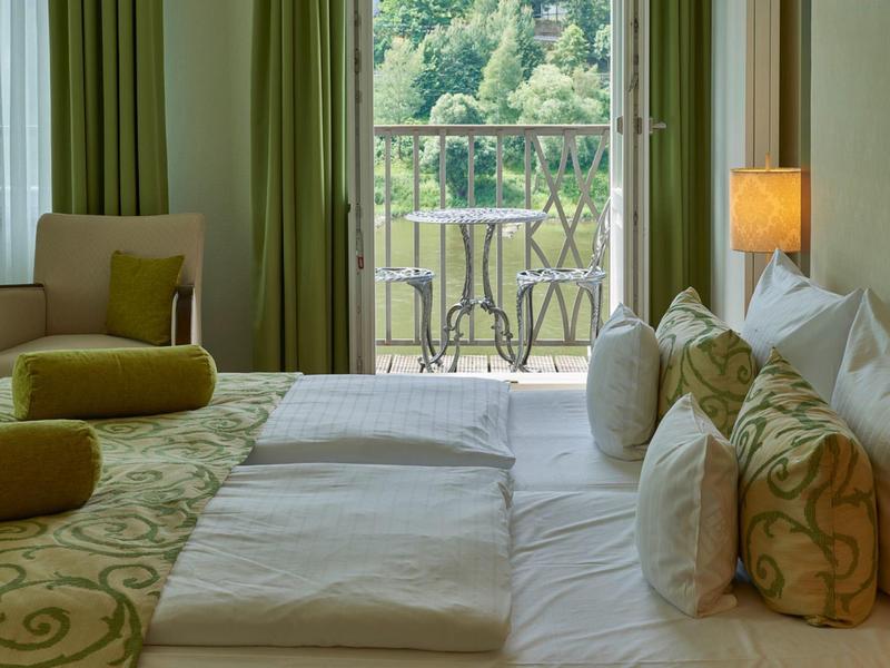 Gemütliches Hotelzimmer mit großen Betten, Sitzbereich und Balkon mit Blick auf grüne Landschaft.