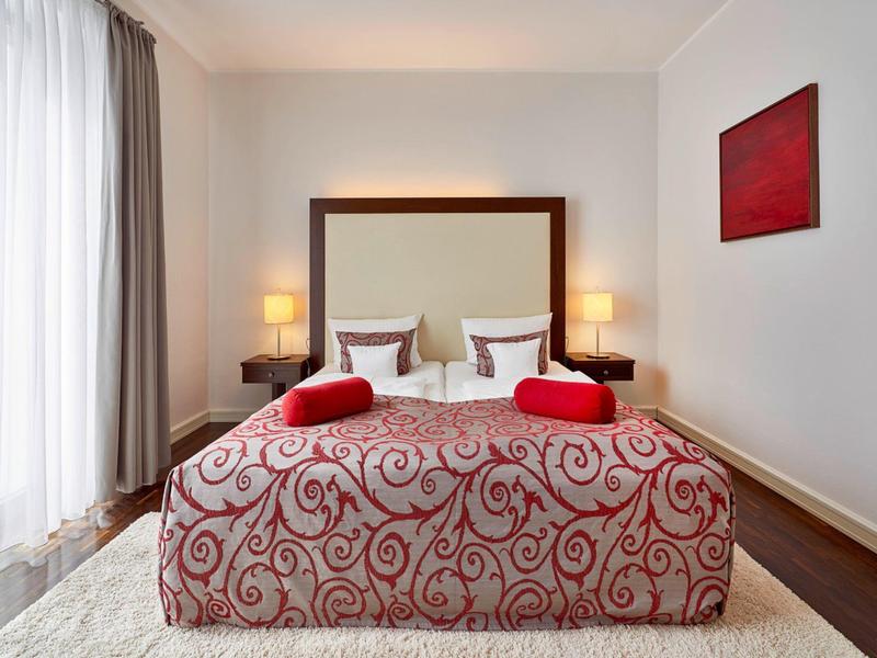 Hotelzimmer mit Doppelbett, zwei Nachttischen mit Lampen und roter Dekoration.