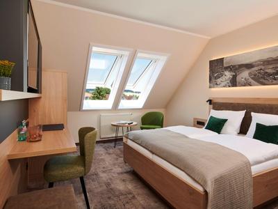 Modernes Schlafzimmer mit Schrägdach, Doppelbett, Schreibtisch und zwei Dachfenstern mit Ausblick.