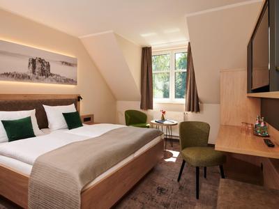 Modern eingerichtetes Hotelzimmer mit großem Bett, Schreibtisch und Fenster mit grünem Ausblick.