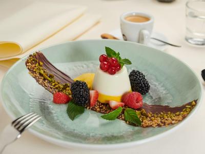 Panna cotta mit Beeren und Granatapfelkernen auf einem hellblauen Teller angerichtet.