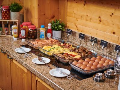 Frühstücksbuffet mit Eiern, Wurst, Käse und Brot in einer Holzumgebung.