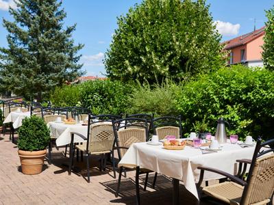 Terrasse eines Hotels mit gedeckten Tischen und Gartenblick bei sonnigem Wetter