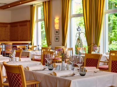 Elegantes Restaurant mit gedeckten Tischen und großen Fenstern mit gelben Gardinen.