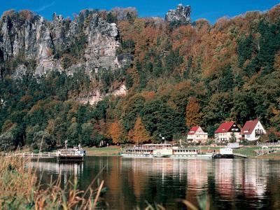 Dorf mit Häusern am Fluss vor bewaldeten Klippen im Herbst.