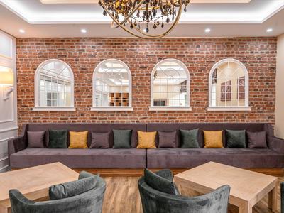 Moderní hotelová lounge s hnědou cihlovou zdí, dlouhou pohovkou a dřevěnými stoly.