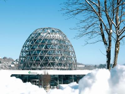 Kugelförmiges Glashaus mit Metallstruktur, umgeben von Schnee und blauen Himmel.