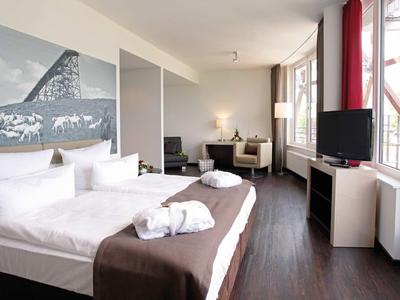 Helles modernes Hotelzimmer mit großem Bett, Sofa, Fernseher und Balkon mit Blick ins Grüne.