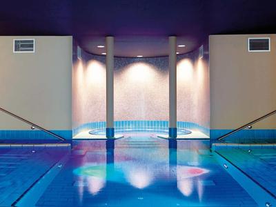 Moderner Innenpool mit Treppen, blauem Wasser, sanfter Beleuchtung und violettem Hintergrund.