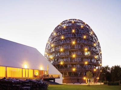 Modernes, kugelförmiges Hotelgebäude neben einem langgestreckten Gebäude bei Dämmerung