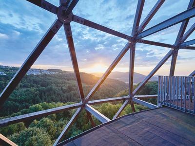 Sonnenuntergang über bewaldeter Landschaft, gesehen durch modernes dreieckiges Metallgerüst.