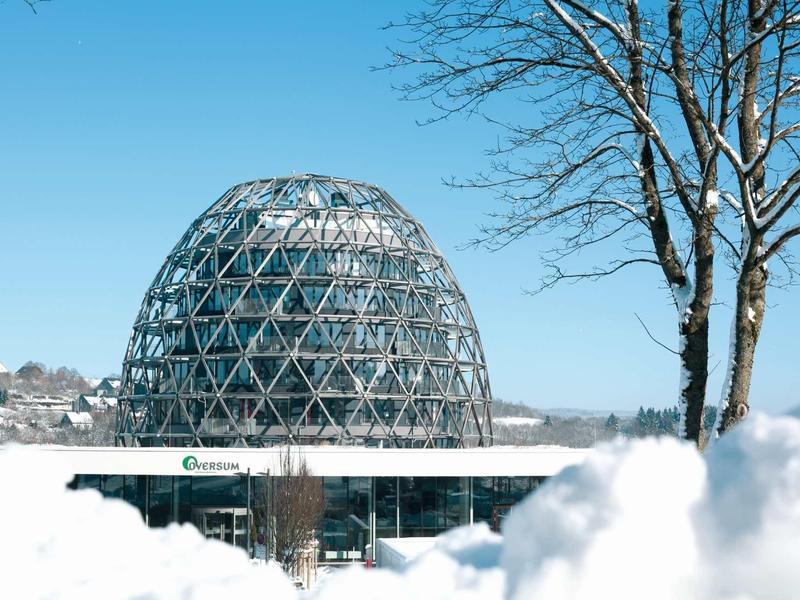 Kugelförmiges Glashaus mit Metallstruktur, umgeben von Schnee und blauen Himmel.