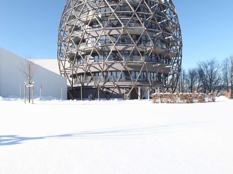 Rundes, gläsernes Gebäude mit Metallgitterkonstruktion im Schnee unter klarem blauem Himmel.