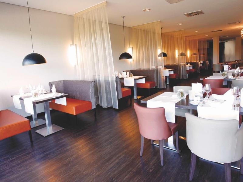 Elegantes Restaurant mit weißen Tischen, orangen und weißen Stühlen, braunem Holzboden und Lampen.