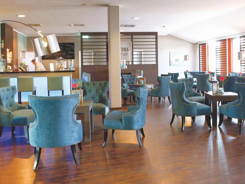 Helles Café mit Holzboden, blauen Polsterstühlen und Tischen mit weißen Tischdecken.