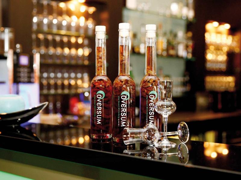 Drei Flaschen Brauner Geist neben einem aufgefüllten Glas auf glänzendem schwarzen Tresen.