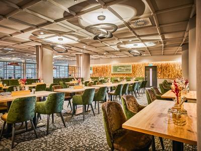 Ein modernes Hotelrestaurant mit Holzvertäfelungen, grünen Sesseln und großen Fenstern.