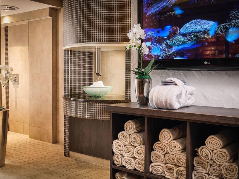 Moderner Wellnessraum mit gestapelten Handtüchern, Blumen und kahlem Licht in warmen Farben.